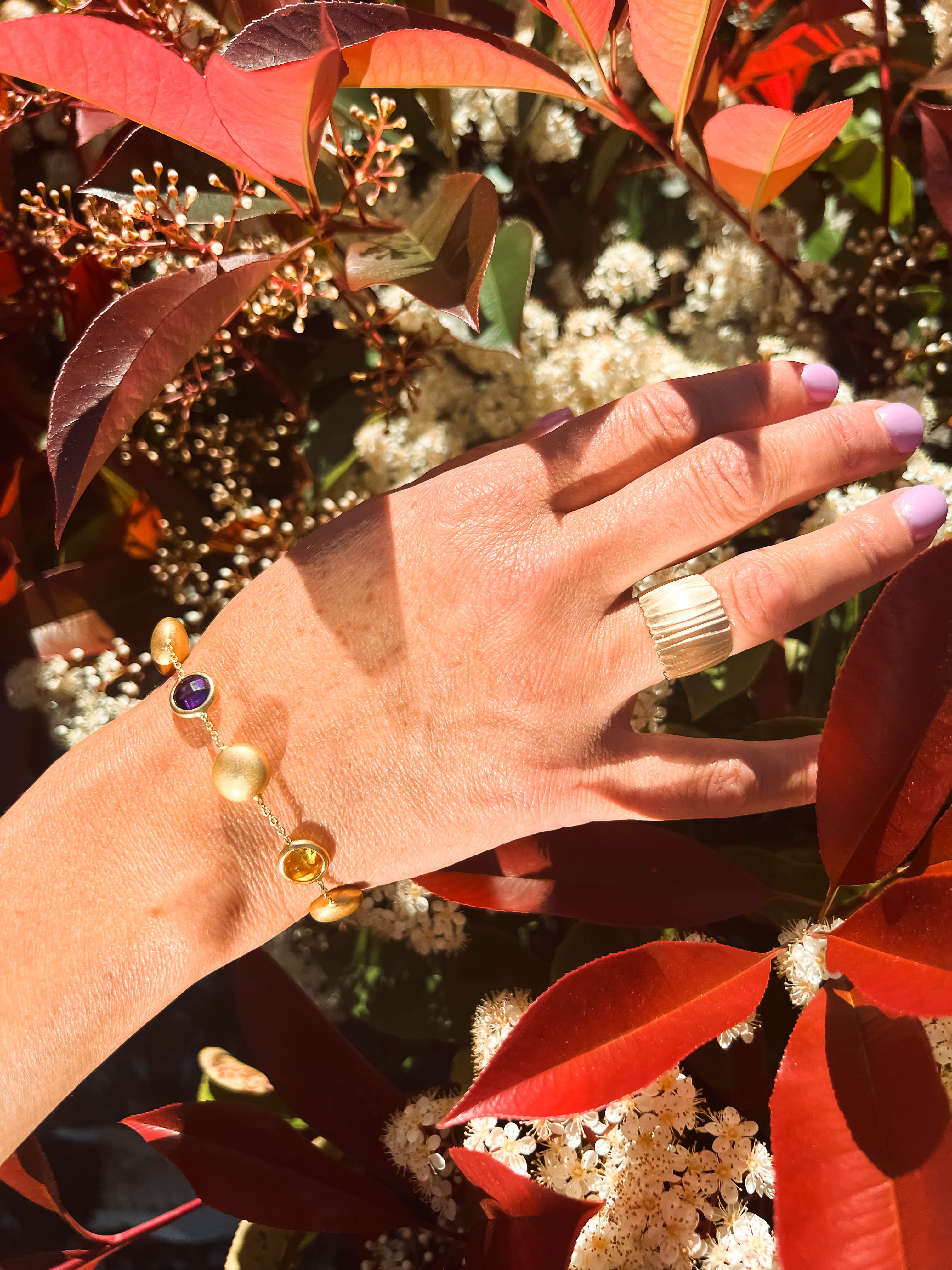 Hand with layered gold bracelets and gemstone details, shown in natural sunlight.