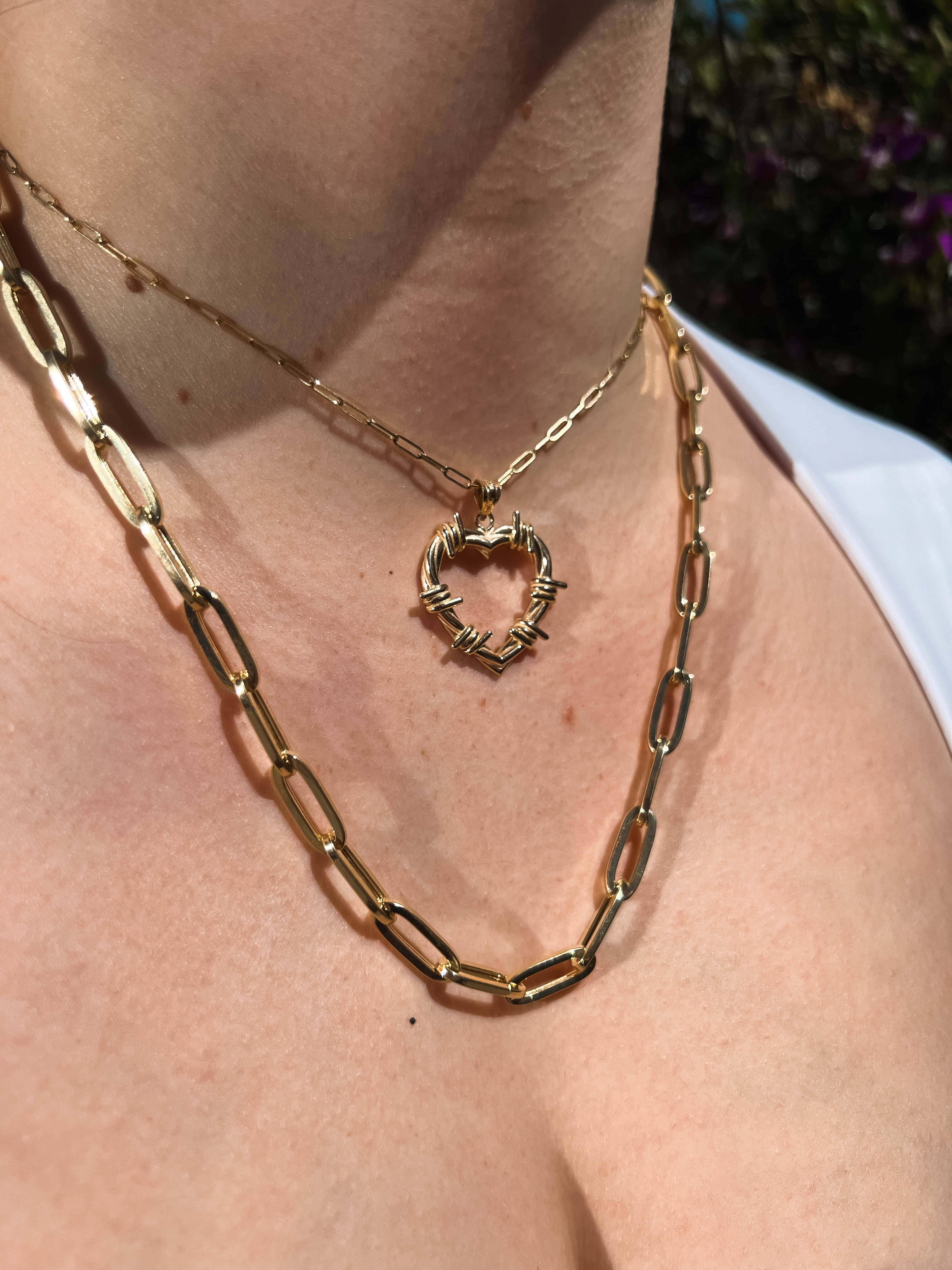 Heart-shaped gold pendant necklace layered with a chunky chain necklace on a woman's chest.